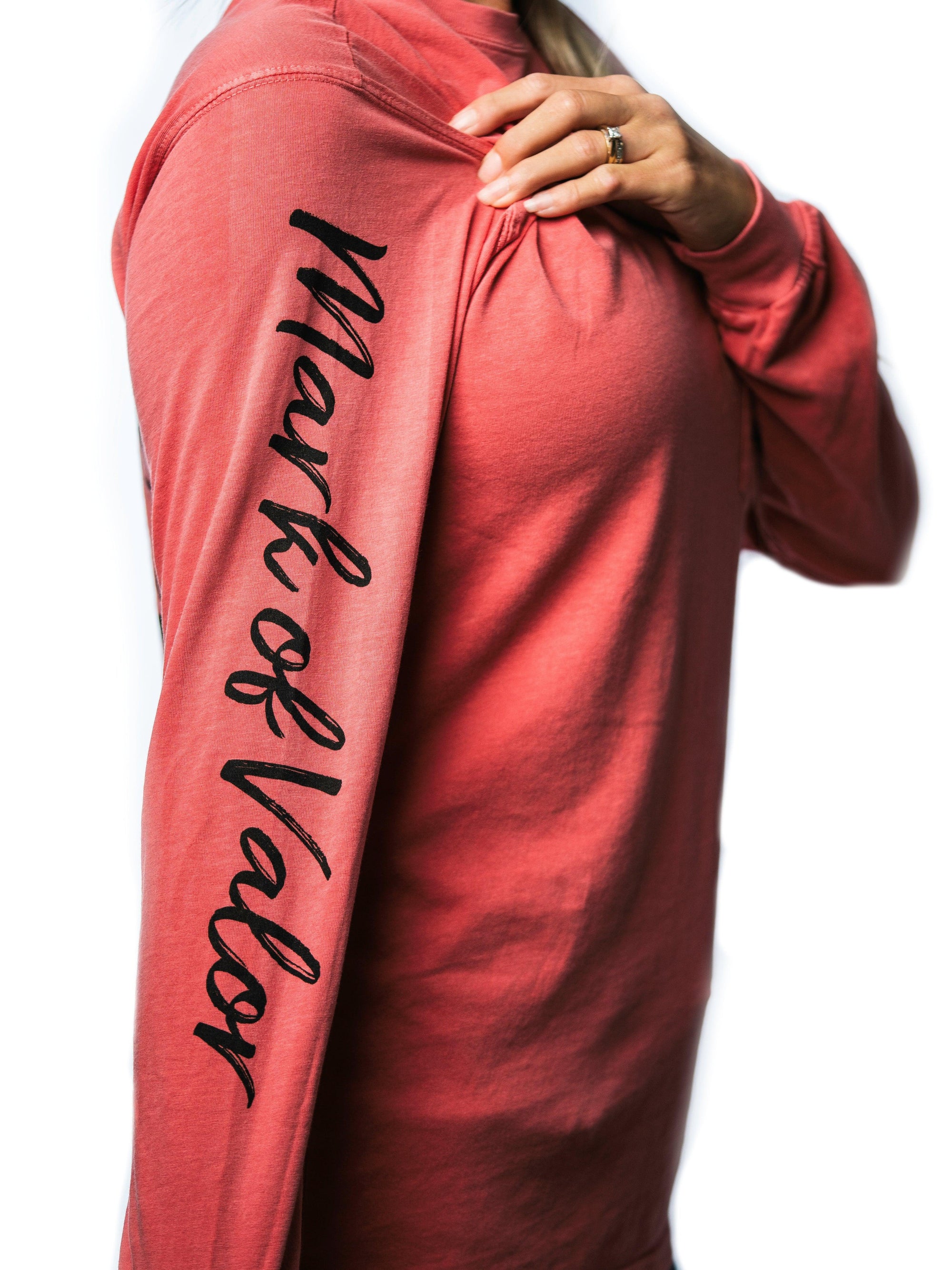 Side view of a woman wearing a pink long-sleeve shirt that has the words “Mark of Valor” printed on the right sleeve